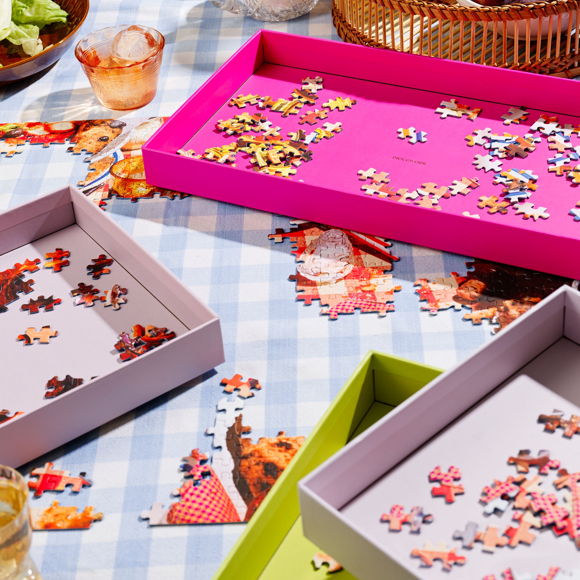 Puzzle Sorting Trays from Piecework Puzzles shown stacked on a table filled with sorted puzzle pieces and assembled sections of puzzle.